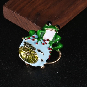 Macro della spilla a rana in smalto verde con strass rossi e dettagli in foglia d'oro