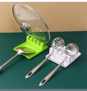 Green and white kitchen tool rests holding lid, spatulas and spoons on a modern countertop