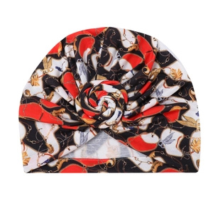 Detail of red black and white turban hat featuring gold chain print and spiral knot