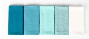 Detail of neatly folded pearl chiffon hijabs in a gradient from dark teal to white