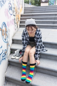 Vibrant rainbow striped crew socks shown on a model against a graffiti street backdrop