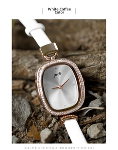 Close-up of elegant oval watch with crystal bezel and white leather strap on natural stones