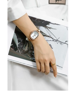 Detail of elegant gold oval watch with small crystals on white strap worn by model
