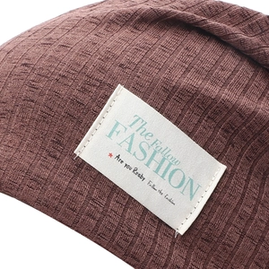 Close-up of dark coffee ribbed knit beanie featuring a white rectangular woven fashion label