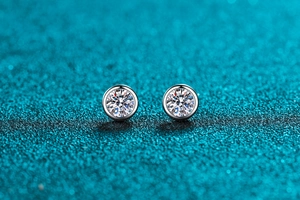 Macro shot of silver round-cut moissanite stud earrings in bezel setting on glitter