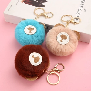 Close-up of three plush teddy bear keychains in blue, beige, and brown with gold metal rings