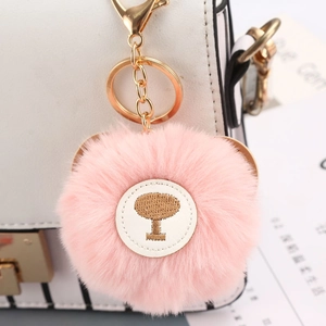 Detailed close-up of a pink plush pompom keychain with gold metal clasp on a handbag
