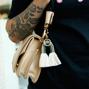 Porte-clés arc-en-ciel tissé main avec pompons bleus et jaunes sur un sac à main beige
