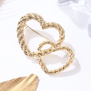 Macro detail of interlocking gold double heart brooch with textured rope finish on white