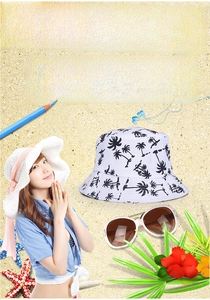 White sun bucket hat with black coconut tree print on beach sand with sunglasses