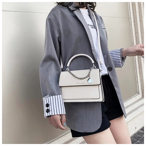 Close-up of minimalist beige handbag featuring silver chain detail and metallic charm