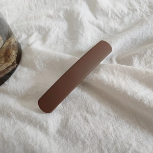 Close-up of a matte dark brown barrette clip on a white textured fabric background