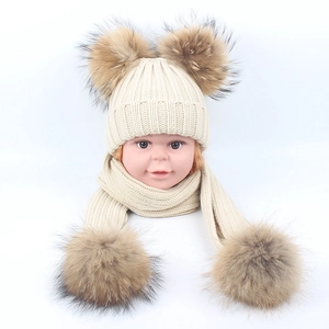 Detail of baby winter knit hat and scarf set featuring oversized faux fur pom-poms