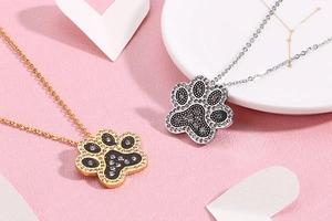 Detail of gold and silver paw print necklaces with sparkling crystals on pink background