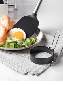 Detail of round non-stick egg mold with handle next to a prepared breakfast