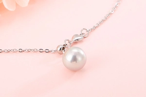 Close-up of stainless steel necklace with round white shell pearl and heart pendant