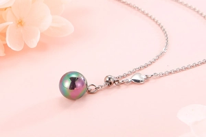 Detail of silver necklace with rainbow pearl pendant and small heart charm on pink floral