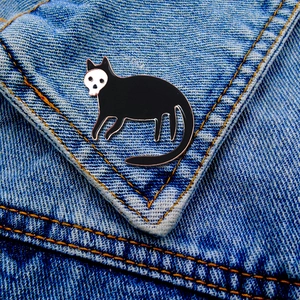 Detail of gothic black cat skeleton enamel pin on a denim jacket pocket