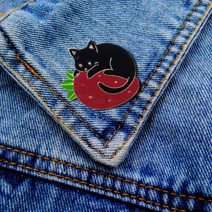Detail of cartoon black cat on strawberry enamel pin brooch on blue denim jacket