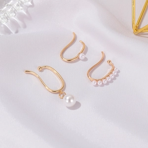 Detailed macro view of three gold pearl ear clips on elegant white silk fabric