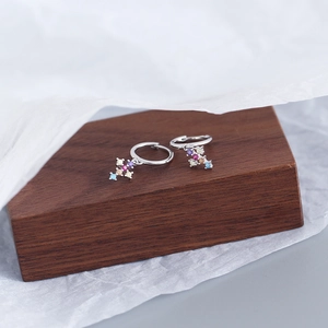Macro shot of silver cross earrings with colorful zircons on a dark wood display