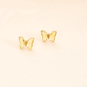 Close-up of yellow crystal butterfly stud earrings with gold plating on warm background