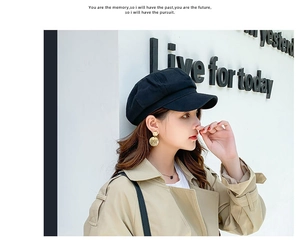 Detail of a black cotton linen octagonal hat worn with a khaki trench coat for an urban look
