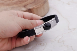 Detail of black leather braided bracelet featuring silver metal plate with centered black gem