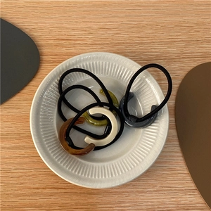 Close-up of C-shaped acetate hair ties in amber and cream on a ceramic dish