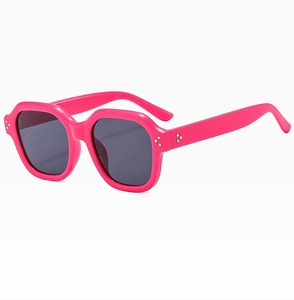Close-up of rose red oversized sunglasses featuring three metal rivets on hexagonal frame