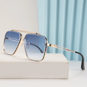Detalle de gafas de sol de metal dorado oversize con lentes degradadas azules en soporte