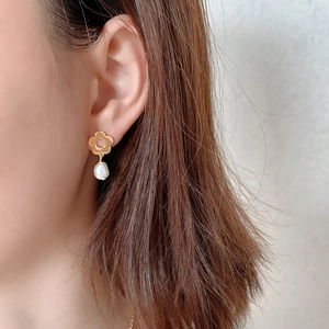 Close-up of model wearing gold flower earrings with white baroque pearl drop charms
