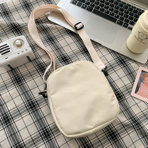 Minimalist beige nylon crossbody bag displayed on a checkered cloth with lifestyle props
