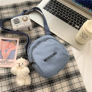 Detail of blue canvas crossbody bag with cute plush bear charm on checkered cloth