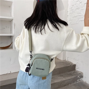 Detail of light green nylon mini crossbody bag with adjustable strap in casual lifestyle setting