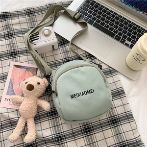 Detail of light green canvas crossbody bag with dark green strap and bear pendant