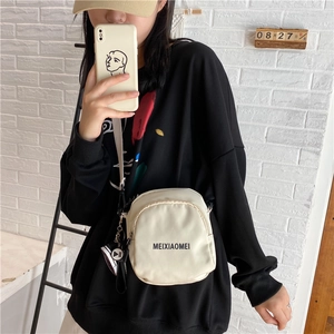 Detail of beige nylon crossbody bag featuring black lettering and sneaker-shaped charm