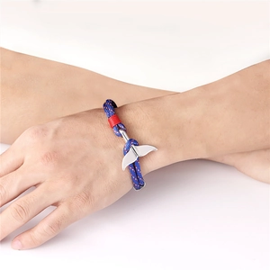 Close-up of blue nylon paracord bracelet featuring a silver whale tail charm and red accents