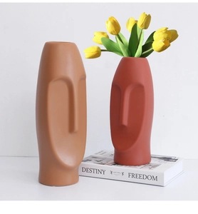 Detail of minimalist ceramic face vases in camel and terracotta with a tulip decoration