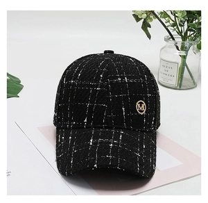 Detail of black tweed baseball cap with white grid pattern and golden metal M logo