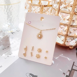 Détail d'un ensemble collier soleil doré et boucles d'oreilles sur carte rose