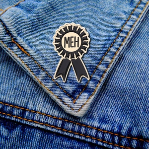 Close-up of a MEH slogan rosette enamel pin badge on a blue denim jacket pocket