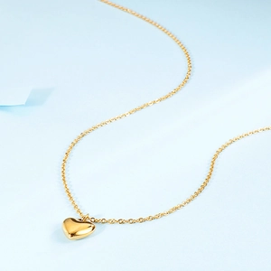 Polished gold heart pendant on a delicate cross chain necklace over blue background