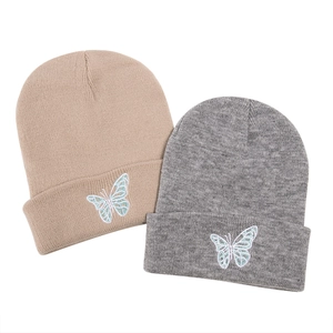 Close-up of butterfly embroidery detail on soft beige and grey knitted beanies