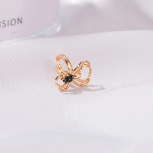 Macro detail of golden spider ear cuff with black drop inlay on white textured background
