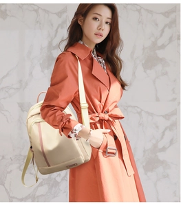 Detalle de mochila de nailon beige con correas marrones llevada por modelo con abrigo naranja