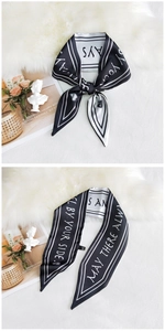 Detail of a black and white twilly silk scarf with letter print and pointed ends on fur