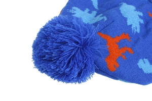 Detail of blue knit beanie featuring orange dinosaur pattern and fluffy pom-pom top
