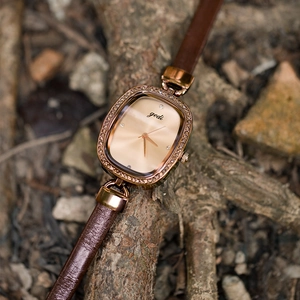 Elegant rose gold oval watch with brown leather strap displayed on a natural branch