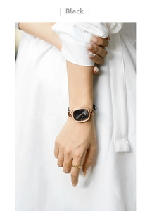 Detail of elegant black oval watch with rhinestones and gold chain ring on wrist